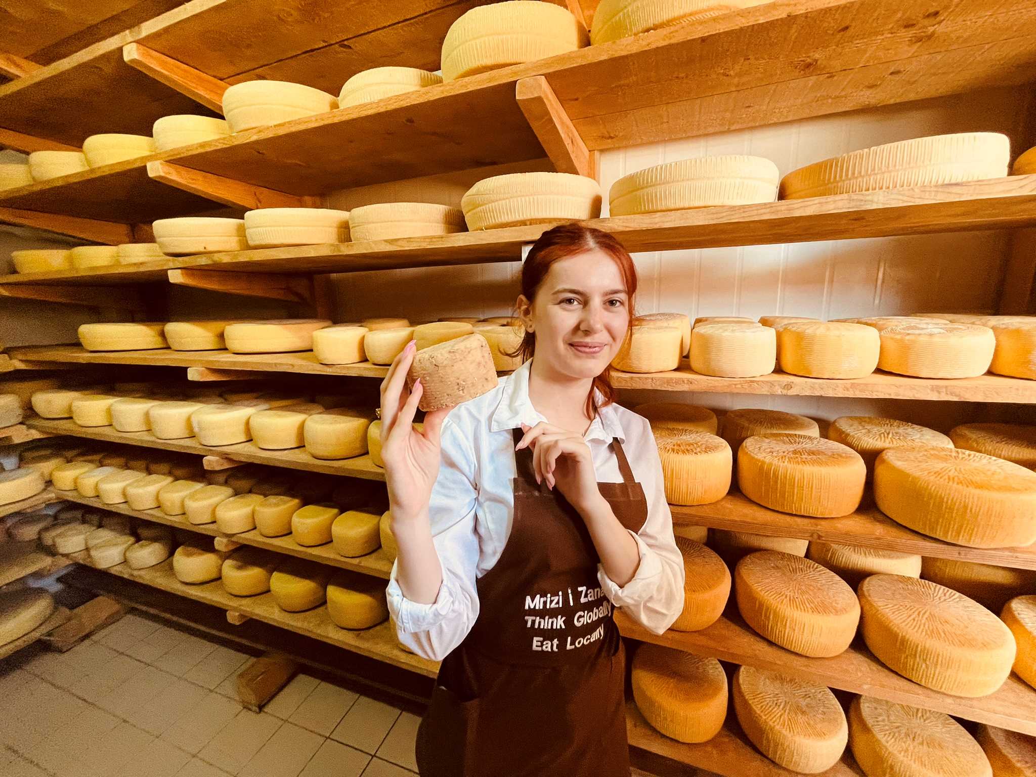 Young female with red hair, holding a block of cheese in a cheese room in Albanian cheese manufacturer